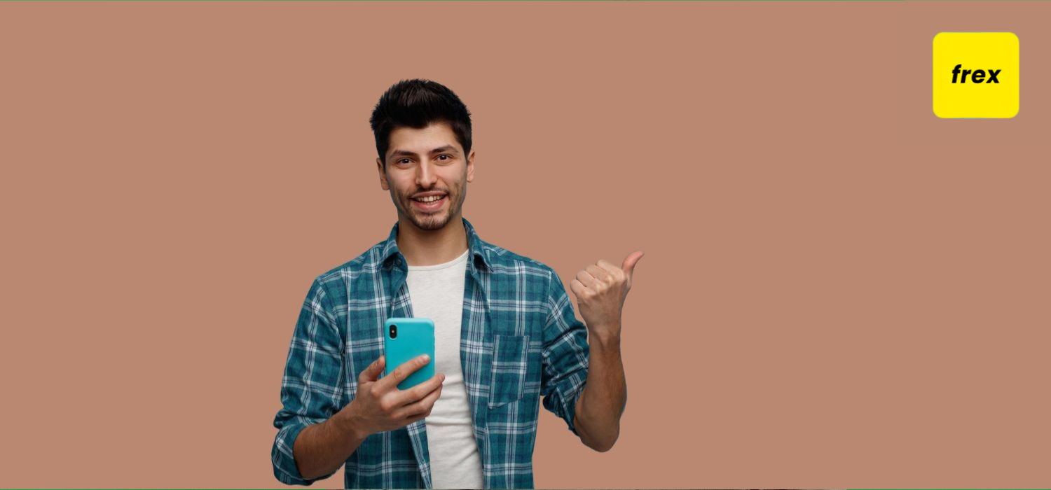 Smiling young man holding mobile phone looking at camera pointing to side