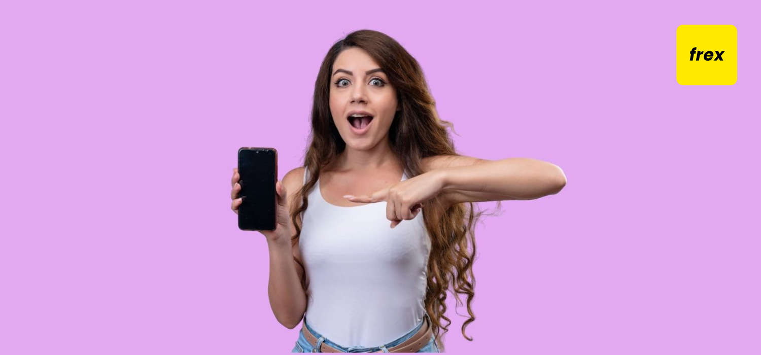 Surprised young beautiful girl holding mobile phone and pointing at it